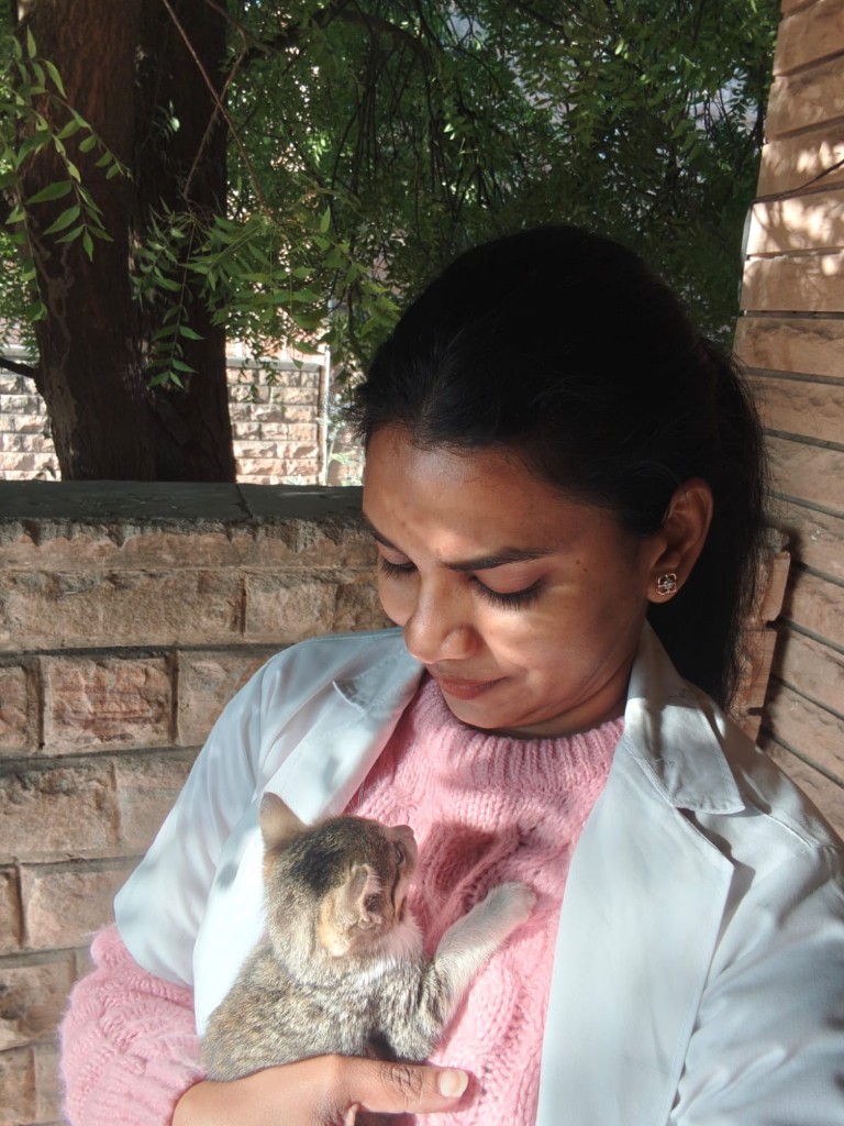 Vandana in a white coat gently holding a small tabby kitten in her arms