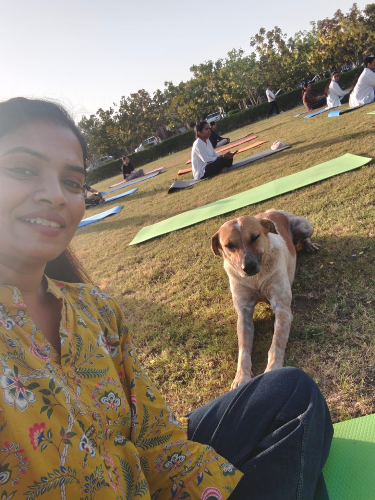 Vandana smiling in a selfie with a calm white and tan stray dog on a grassy field
