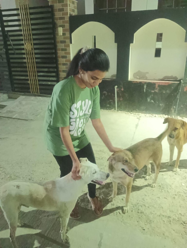 Vandana smiling while petting three rescue dogs at night