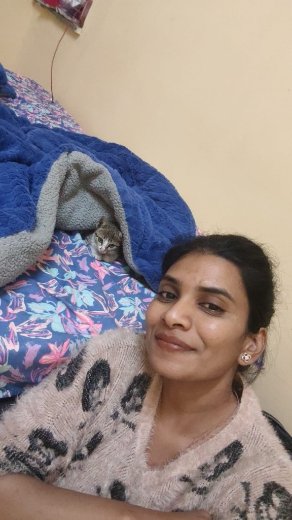 Vandana taking a selfie with a tabby rescue kitten on a bed